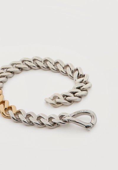 Χοντρό ασημένιο βραχιόλι με μία χρυσή σειρά και ένα κυρτό κούμπωμα με χαραγμένη την επιγραφή "RAINBOW K 925 14K" σε λευκό φόντο.