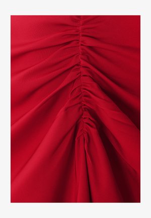 Punane kangas, millel on vertikaalne rüüs, luues tekstuuri. Materjal näib ehk pehme ja kerge, sujuva ja voolava langusega.