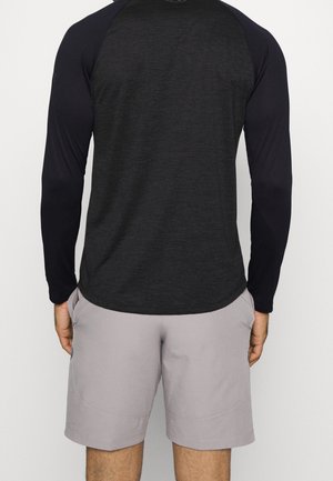 Langärmliges Sportshirt aus dunkelgrauem Stoff mit schwarzen Ärmeln, kombiniert mit hellgrauen Shorts; glatte Textur und lässige Passform.