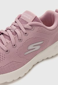 Light pink Skechers sneaker featuring mesh fabric, rounded toe, lace-up closure, and a white rubber sole with logo accent.