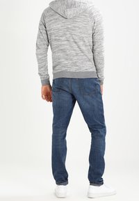 Hoodie gris texturé avec une capuche, associé à un jean bleu. Des baskets blanches complètent la tenue. Vue de dos, montrant l'ajustement et le design.