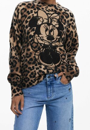 Personne portant un pull à motif léopard avec un grand contour noir de Minnie Mouse à l'avant et un jean bleu clair avec de petites patchs brodées.