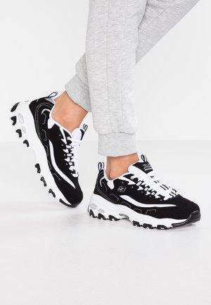 Des chaussures de sport noir et blanc en maille et suède, avec une semelle épaisse, des lacets blancs et un logo sur le côté.