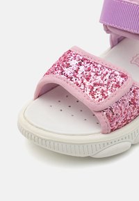 Rosa glitter sandaler med bred rem, myke rosa detaljer, hvit teksturert såle og borrelås lukking. Har små perforeringer i sålen.