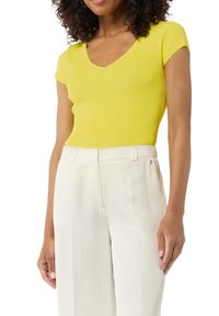 Żółta, prążkowana bluzka krótki rękaw z dekoltem w kształcie litery V, w zestawieniu z białymi, dopasowanymi spodniami o wysokim stanie z delikatnym akcentem po bokach.