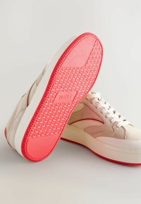Sneaker beige con tomaia in suede morbido, lacci bianchi e suola in gomma rosa texturizzata con un motivo di battistrada e il marchio "NEXT".