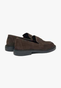 Brązowe zamszowe loafersy z płaską czarną podeszwą, z detalem w postaci złożonego paska i zaokrąglonym noskiem; gładka tekstura i minimalistyczny design.