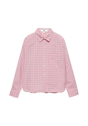 Personne aux longs cheveux bouclés portant une chemise ample à carreaux roses avec une petite étiquette rectangulaire dans le haut du dos.