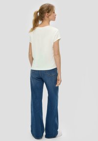 Biała bluzka z krótkim rękawem połączona z niebieskimi dżinsami flare o wysokim stanie. Dżinsy mają subtelne przeszycia i tylne kieszenie, a całość uzupełniają białe sneakersy.