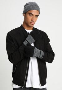 Black suede bomber jacket, white T-shirt, gray knit beanie, gray-black striped gloves with finger coverage, textured fabric accents.