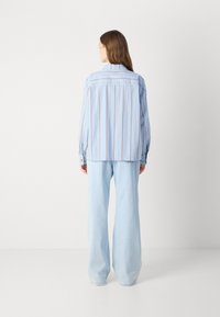 Light blue striped shirt with long sleeves and a relaxed fit, paired with light blue wide-leg jeans. Cotton fabric with contrasting stripes.