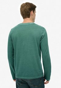 Camiseta de manga larga verde, material de algodón, cuello redondo, acabado texturizado, estilo ajustado, con dobladillo recto y diseño sencillo.