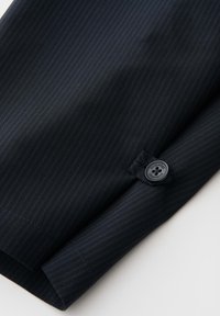Dark pinstripe suit sleeve with a black button sewn near the cuff, showing fabric texture and fine stitching details.