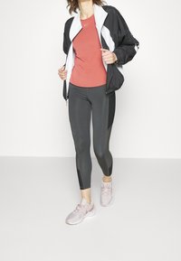 Conjunto deportivo que incluye una chaqueta de cremalleras en blanco y negro, camiseta roja, mallas negras con paneles de malla y zapatillas de deporte rosa claro.