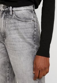 Šedé džíny z denimu s bledým vzorem, s vysokým pasem, předními kapsami a štíhlým střihem. Ozdobeny měděným kováním.