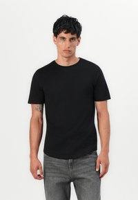 Black cotton t-shirt with short sleeves, crew neck, and a fitted design. Worn with gray denim jeans, featuring a smooth texture.
