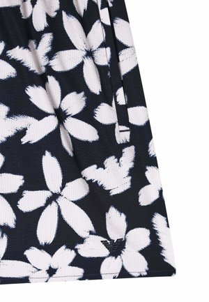 Gros plan sur un tissu foncé avec un grand motif floral blanc et un petit logo près du bord inférieur.