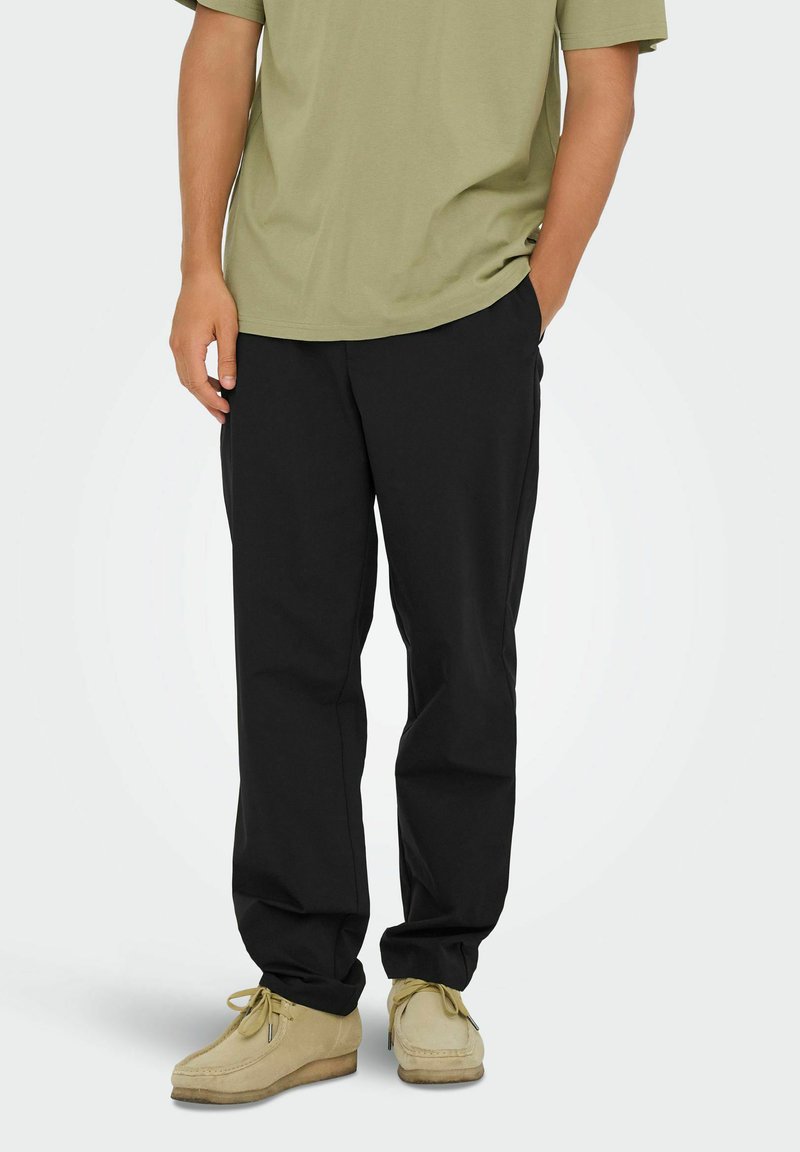 Black, relaxed-fit trousers made of lightweight material, paired with a light green T-shirt and beige suede shoes. Simple design, no visible patterns.
