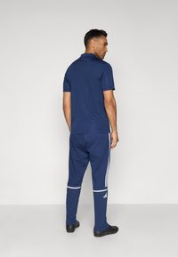 Camisa polo azul marino y pantalones de chándal, ambos en una tela suave. Los pantalones tienen franjas blancas a lo largo de los lados y un logo cerca del tobillo.