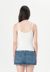 Top blanco de canalé con tirantes finos y falda corta de mezclilla azul. La falda cuenta con dos bolsillos traseros y un dobladillo deshilachado.