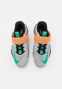 Zapatillas deportivas grises con acentos negros y un Swoosh turquesa, con correas naranjas y superiores texturizados con perforaciones para una mejor transpirabilidad.