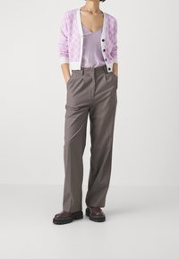 Světlofialový svetr s bílými akcenty a knoflíky, vrstvený přes levandulové tričko. Šedé kalhoty s vysokým pasem a robustní tmavé boty.