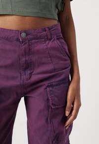 Paarse cargo broek met knoopsluiting, zijzakken en een relaxte pasvorm. De stof lijkt lichtjes textuur te hebben en versleten.