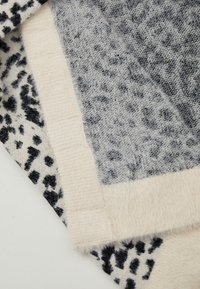 Mjukt stickat tyg med svart och gråt leopardmönster och beige ribbade kanter vikt på en vit yta.