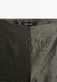 Gros plan sur un tissu gris foncé à rayures verticales avec une couture centrale et une étiquette "Massimo Dutti" à la ceinture.