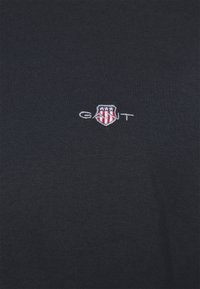 T-shirt noir en coton avec un petit logo brodé représentant des étoiles et des rayures. Texture lisse et design classique à col rond.