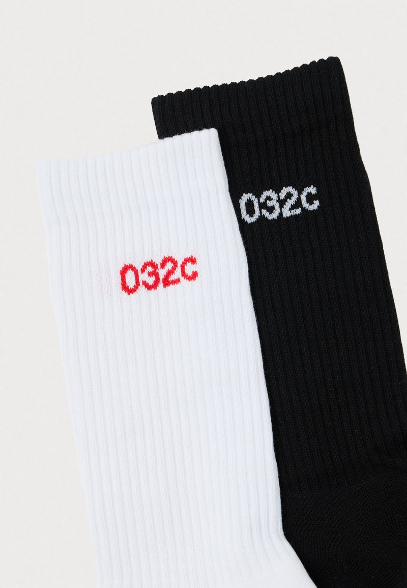 Bomuldsribbet sokker i hvid og sort. Har røde og grå "032c" branding på hver, med kontrastfarver.