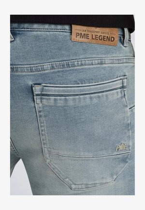 Jean en denim bleu clair avec une patch arrière portant la mention "PME LEGEND," des coutures marquées et un design de poche arrière distinct.