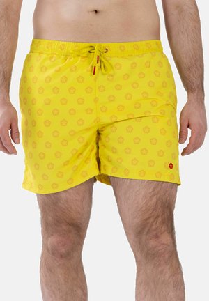 Mann trägt gelbe Badeshorts mit dezentem Blumenmuster und Kordelzug in der Taille, ab Taille bis über die Knie gezeigt.