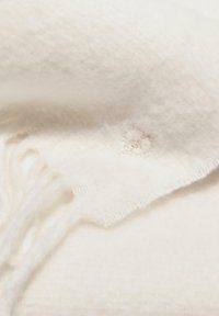 Châle blanc tissé avec une texture douce, des bords de fringes et une petite tache circulaire sur le tissu près du bas.