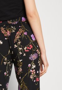 Černé květované kalhoty s živým vzorem růžových a fialových květin se zelenými stonky. Elastický pas a volný střih, vyrobené z měkké látky.