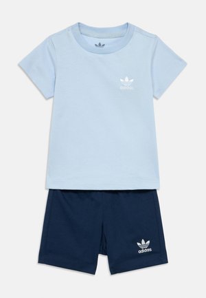 Camiseta de algodón azul claro con mangas cortas y logo de Adidas blanco; combinada con pantalones cortos de algodón azul marino con logo blanco en la pierna.