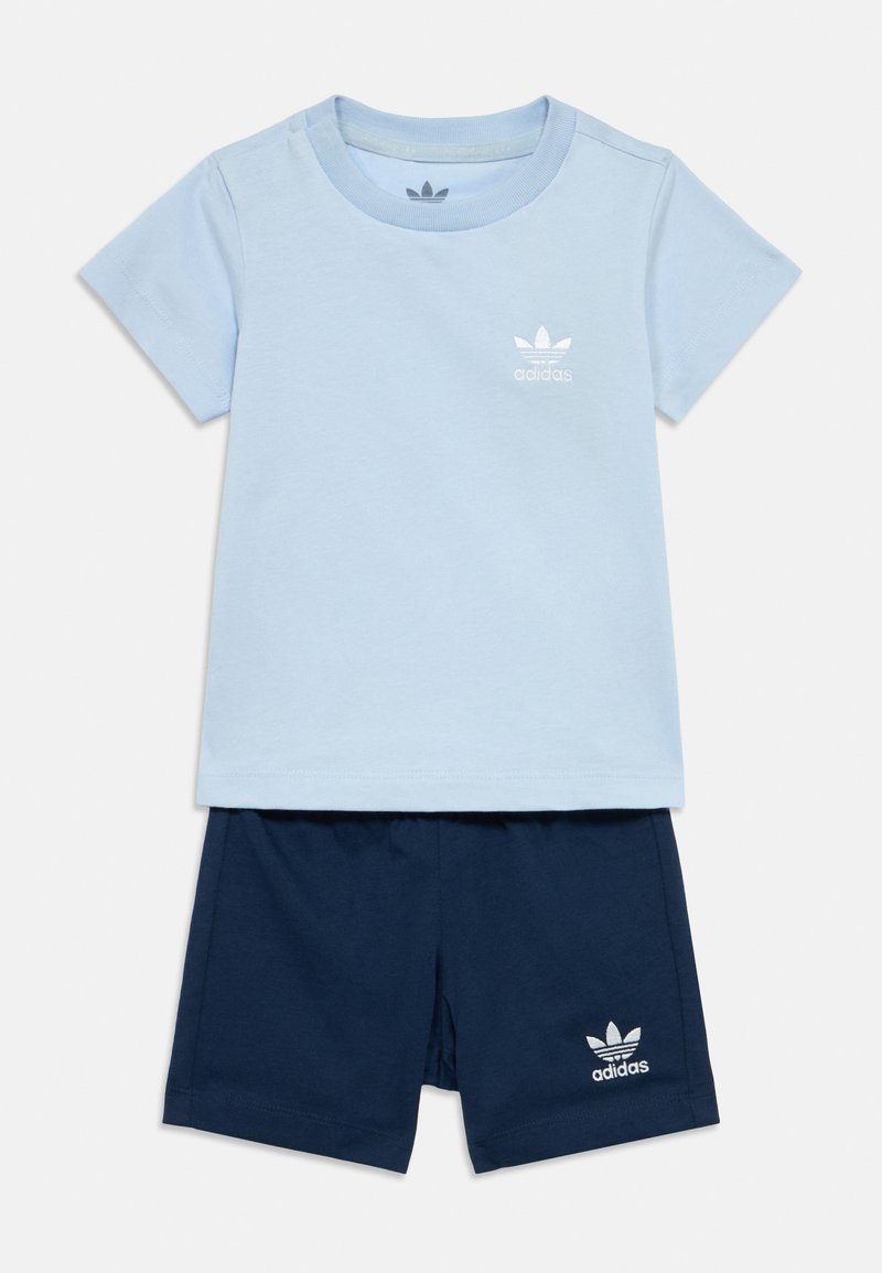 Világoskék pamut póló rövid ujjakkal és fehér Adidas logóval; sötétkék pamut rövidnadrággal, melyen fehér logó található a lábszáron.