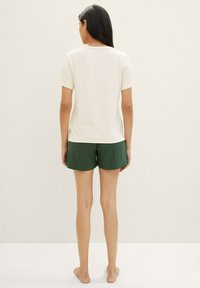 Crèmekleurig shirt met korte mouwen en donkergroene shorts. Het shirt heeft een ronde halslijn; de shorts zijn losjes gesneden en hebben een gladde textuur.
