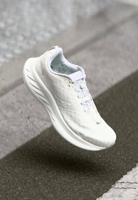 Weißer Sportschuh mit strukturiertem Obermaterial, leichtem Design, gewölbter Sohle und Schnürung vorne. Verfügt über ein Logo an der Seite und einen gepolsterten Schaft.