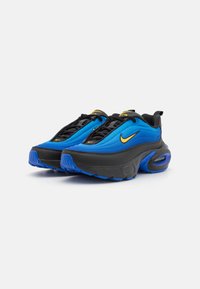Sneakers Nike con una toma blu e accenti neri, lacci neri e un grande swoosh giallo. Hanno una suola nera spessa e dettagli blu.