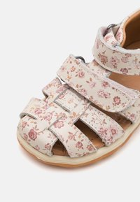 Remmar sandal med ljus blommönster, beige syntetisk ovandel, justerbara kardborreband, vadderad innersula och gummiyttersula.