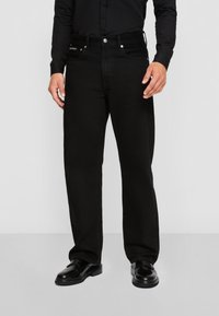 Jeans de denim negro con un ajuste de pierna recta, que cuentan con cinco bolsillos, herrajes en plata y un diseño limpio y minimalista. Acabado de tela texturizada.