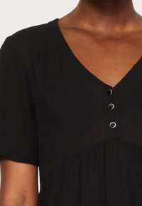 Vestido corto negro de manga corta con un profundo escote en V y tres botones metálicos circulares en el escote, presenta una tela texturizada y una silueta fluida.