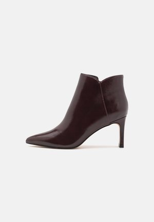 Stivale alla caviglia in pelle borgogna con punta affilata e tacco alto e sottile; presenta un design alto e una consistenza liscia e lucida.