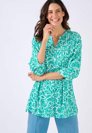 Blusa ligera turquesa con estampado floral, diseño con frente plisado, detalle de botones y mangas de tres cuartos. Combinada con denim claro.