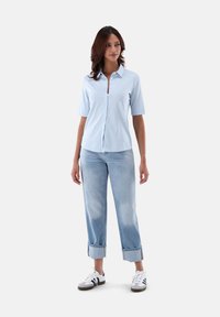 Light blue short-sleeve button-up shirt, paired with rolled-cuff light denim jeans and white sneakers with dark accents.
