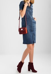 Denim-shirtin mekko lyhyillä hihoilla, keskipitkä, kahdella etutaskulla. Yhdistetty pieneen punaisiin ja oransseihin olkalaukkuun sekä viininpunaisiin korkokenkiin.