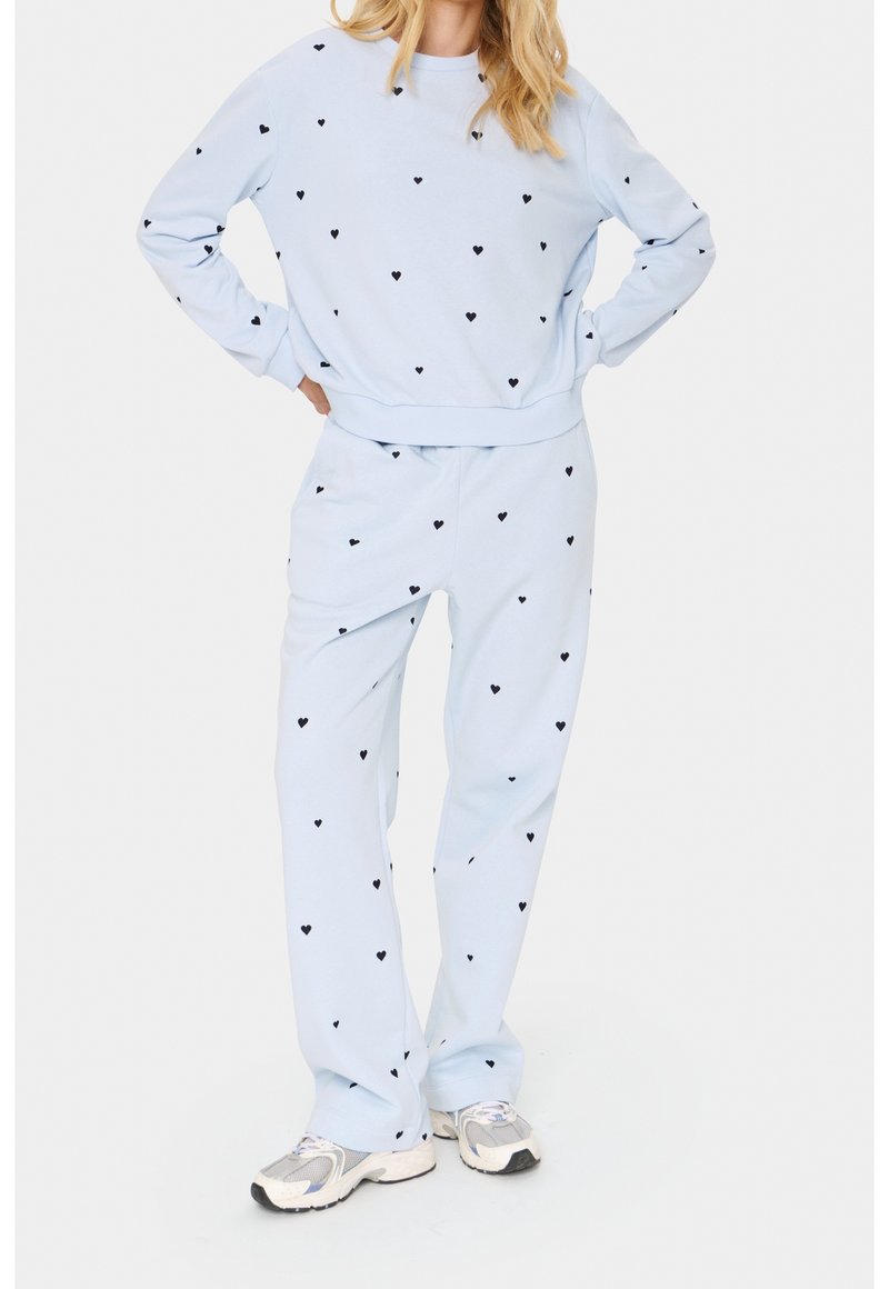 Set composto da felpa e pantaloni azzurro chiaro con piccoli motivi a cuore neri. Tessuto morbido, polsini e vita elasticizzati. Vestibilità casual e design confortevole.