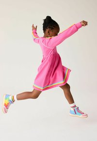 Abito rosa con strisce arcobaleno all'orlo e sulle maniche; abbinato a sneaker alte multicolori e calze bianche alla caviglia con strisce.