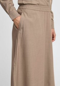 Falda de cintura elástica en color beige con bolsillos laterales, hecha de una tela suave; presenta un corte recto y una sutil textura.